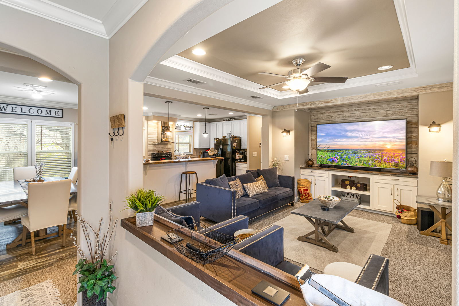 Open-concept living room with a navy sofa, tray ceiling, and adjoining kitchen